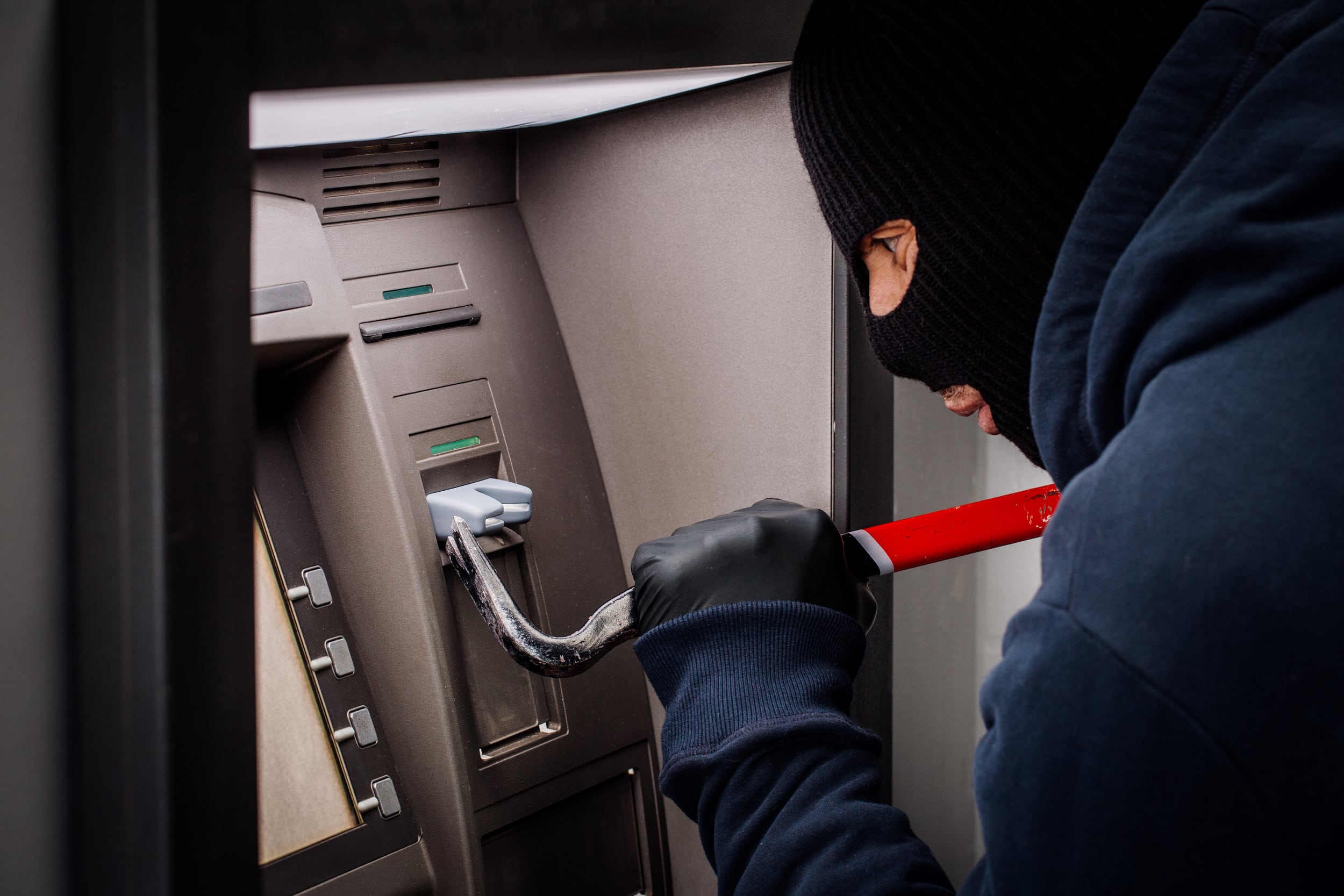 thief with crowbar opens the ATM.